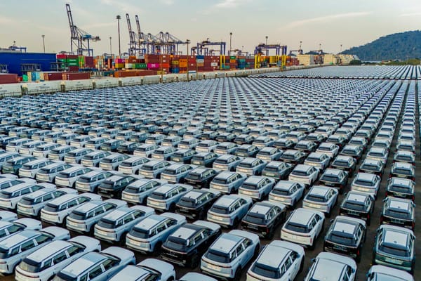 Pátio do Porto de Paranaguá tomado por carros importados, com guindastes de contêineres ao fundo