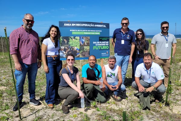 Equipe do IAT posa ao lado de placa de área em recuperação ambiental na restinga