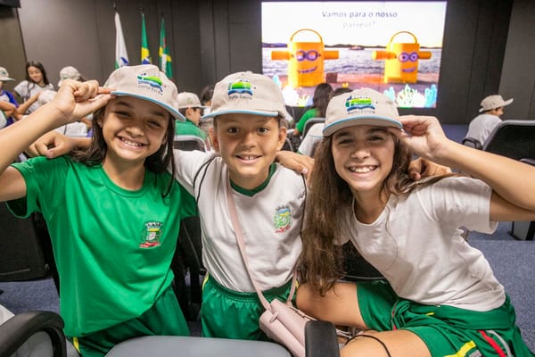 Três alunas de boné sorriem durante a visita do projeto Porto Escola